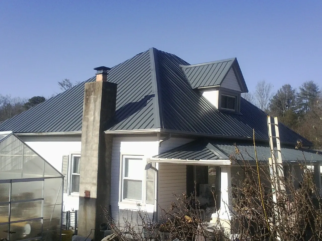 Dark blue standing seam metal roof on a white farmhouse with dormer — Slate & Tile Roof Repair by Roofing Brothers in Wyoming