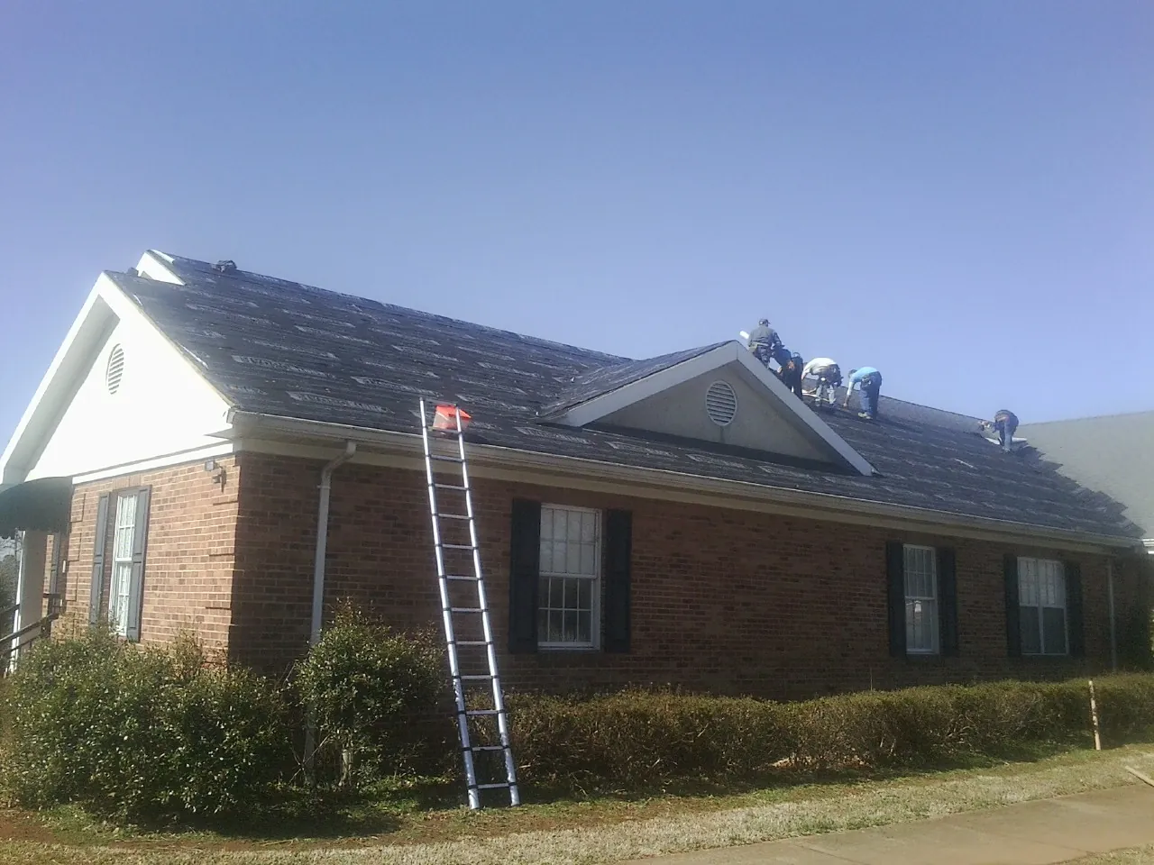 Crew tearing shingles off a brick ranch roof with a ladder set — Emergency Roof Repair work by our crew in Wyoming